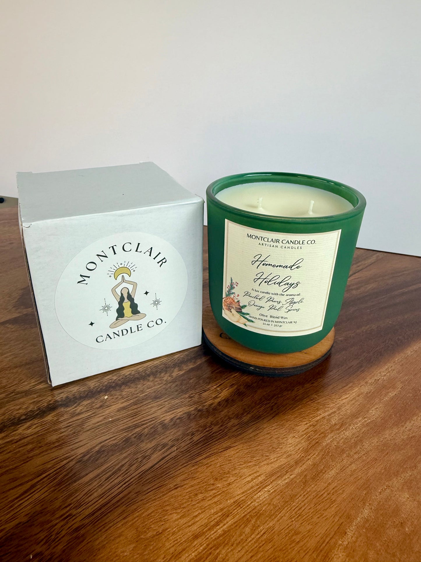 Green candle with a label and white box on a wooden surface, featuring Montclair Candle Co branding.