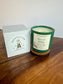 Green candle with a label and white box on a wooden surface, featuring Montclair Candle Co branding.