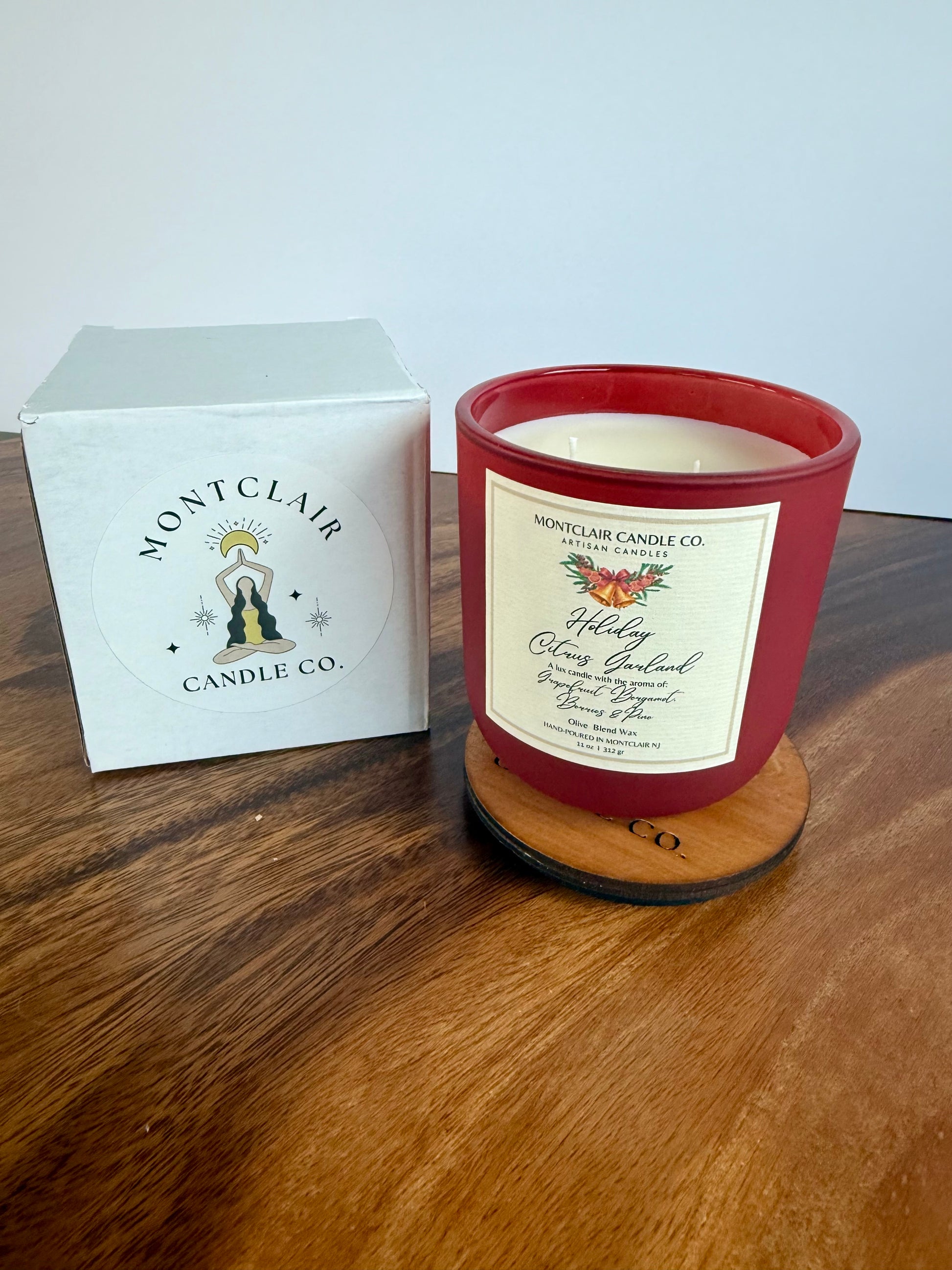 Red candle with a label and Montclair Candle Co. box on a wooden surface