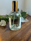 Clear glass bottle with gold cap on a wooden surface with greenery