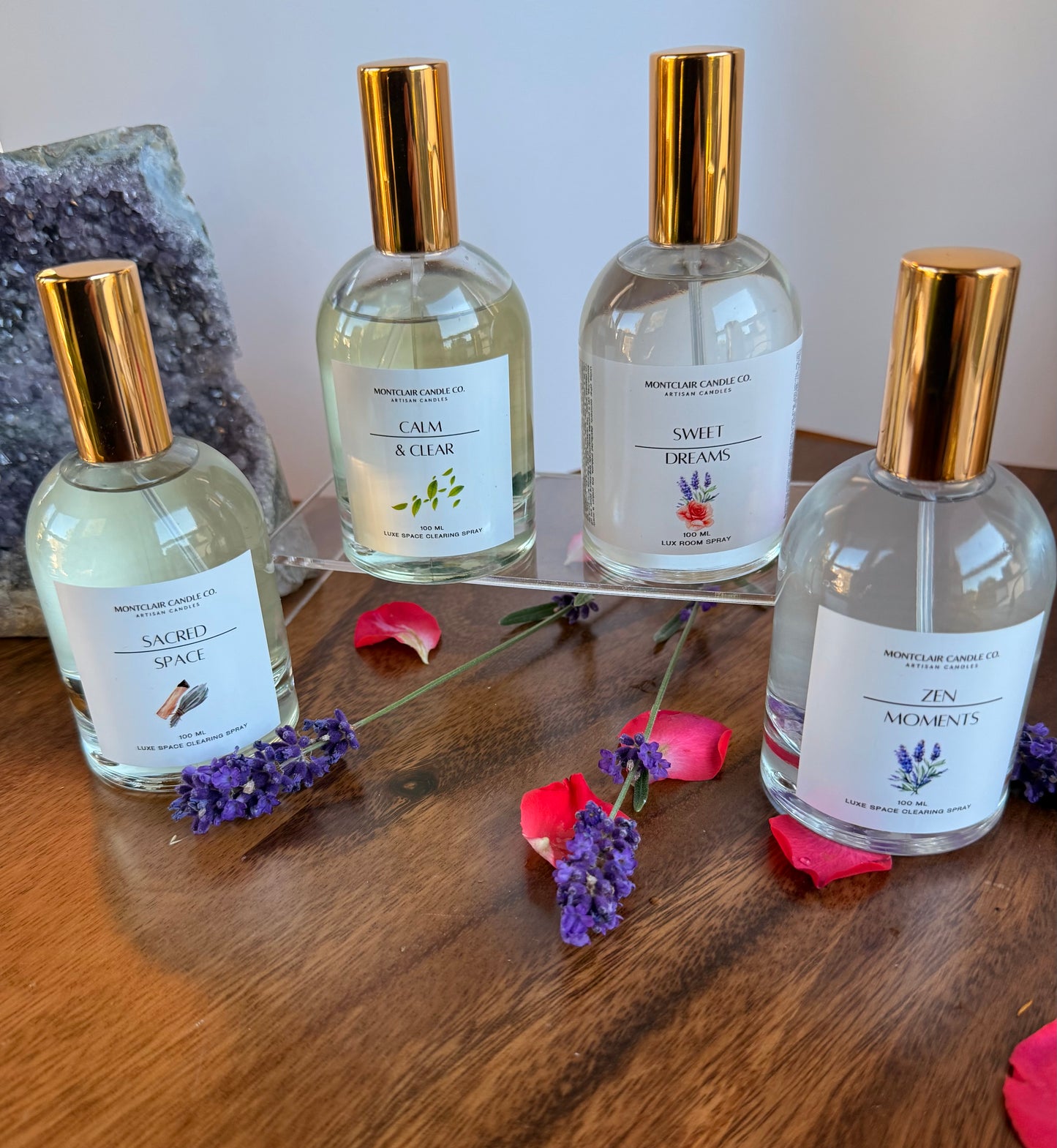 Four bottles of diffuser with gold caps on a wooden surface with flowers and crystals.