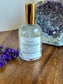 
Back of bottle with gold cap on a wooden surface next to lavender flowers and a crystal formation.