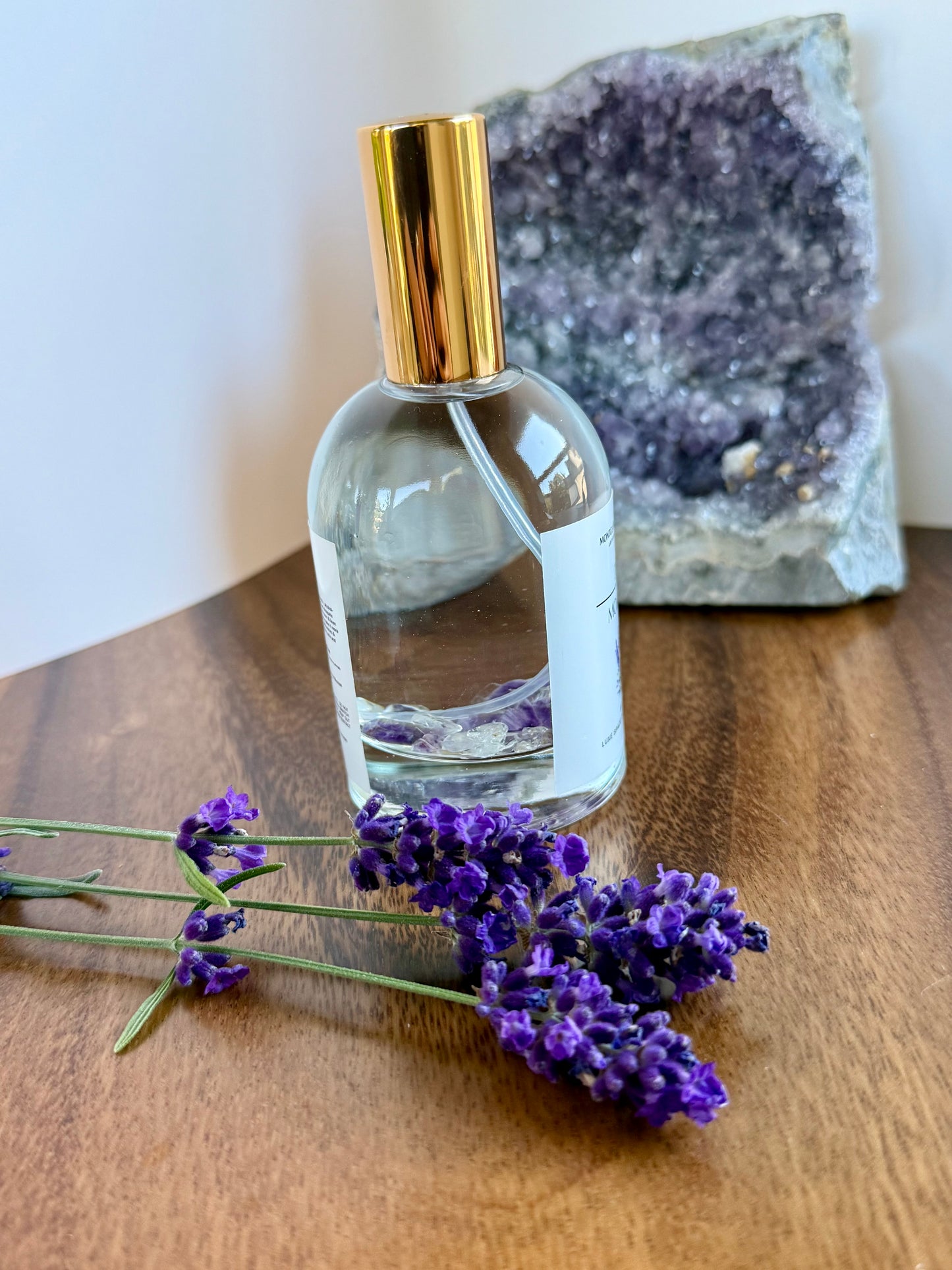 Clear bottle with gold cap on a wooden surface with lavender flowers and a geode in the background
