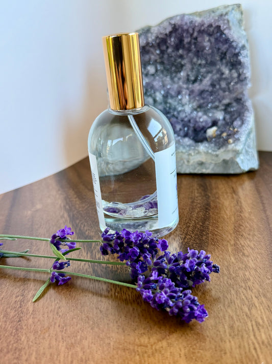 Clear bottle with gold cap on a wooden surface with lavender flowers and a geode in the background