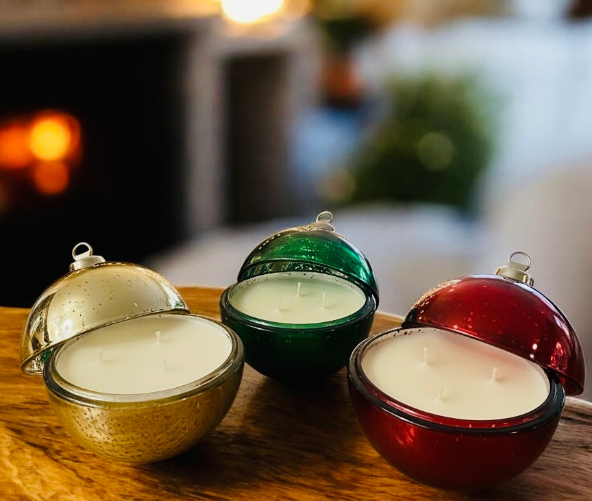 Three spherical candles in metallic containers on a wooden surface with a blurred background