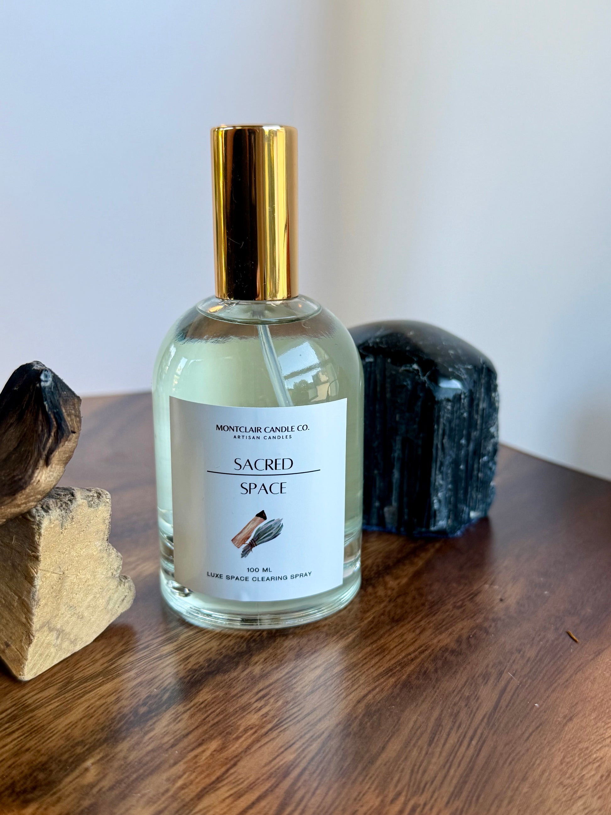 Bottle of 'Sacred Space' diffuser on a wooden surface with decorative stones.