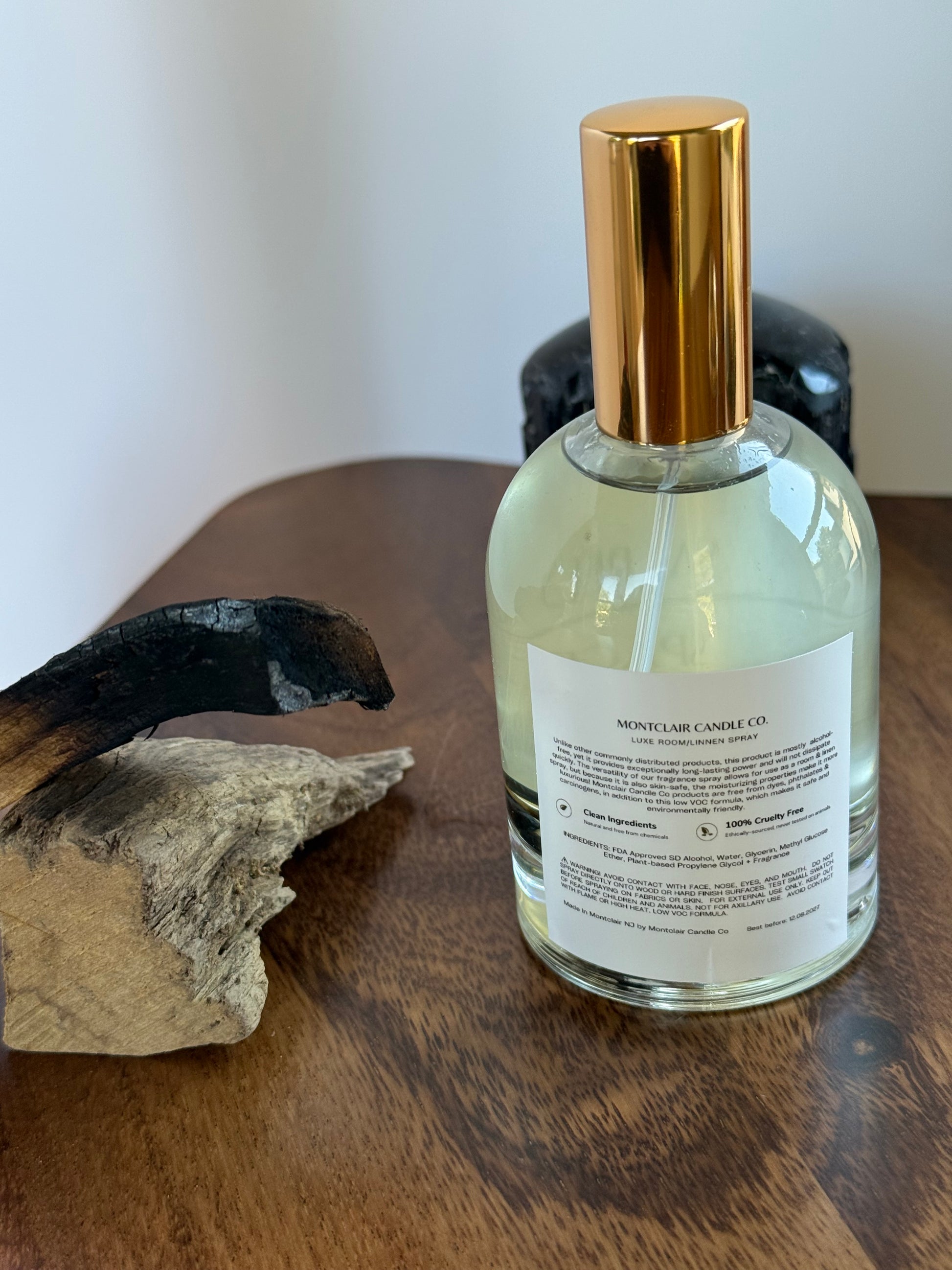 Back of bottle of room spray with a gold foil top on a wooden surface