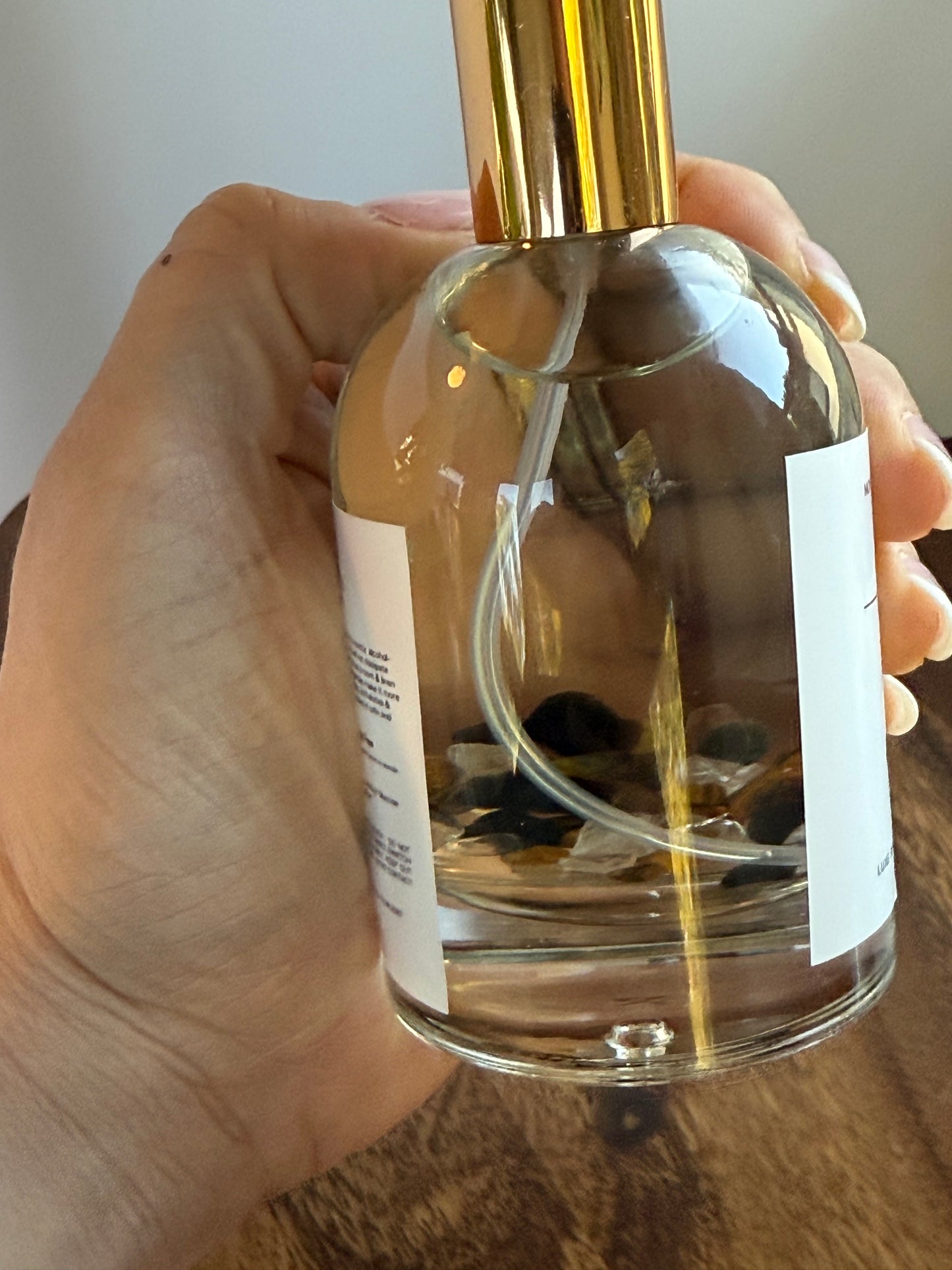 Hand holding a clear glass bottle with a gold cap, filled with a liquid.