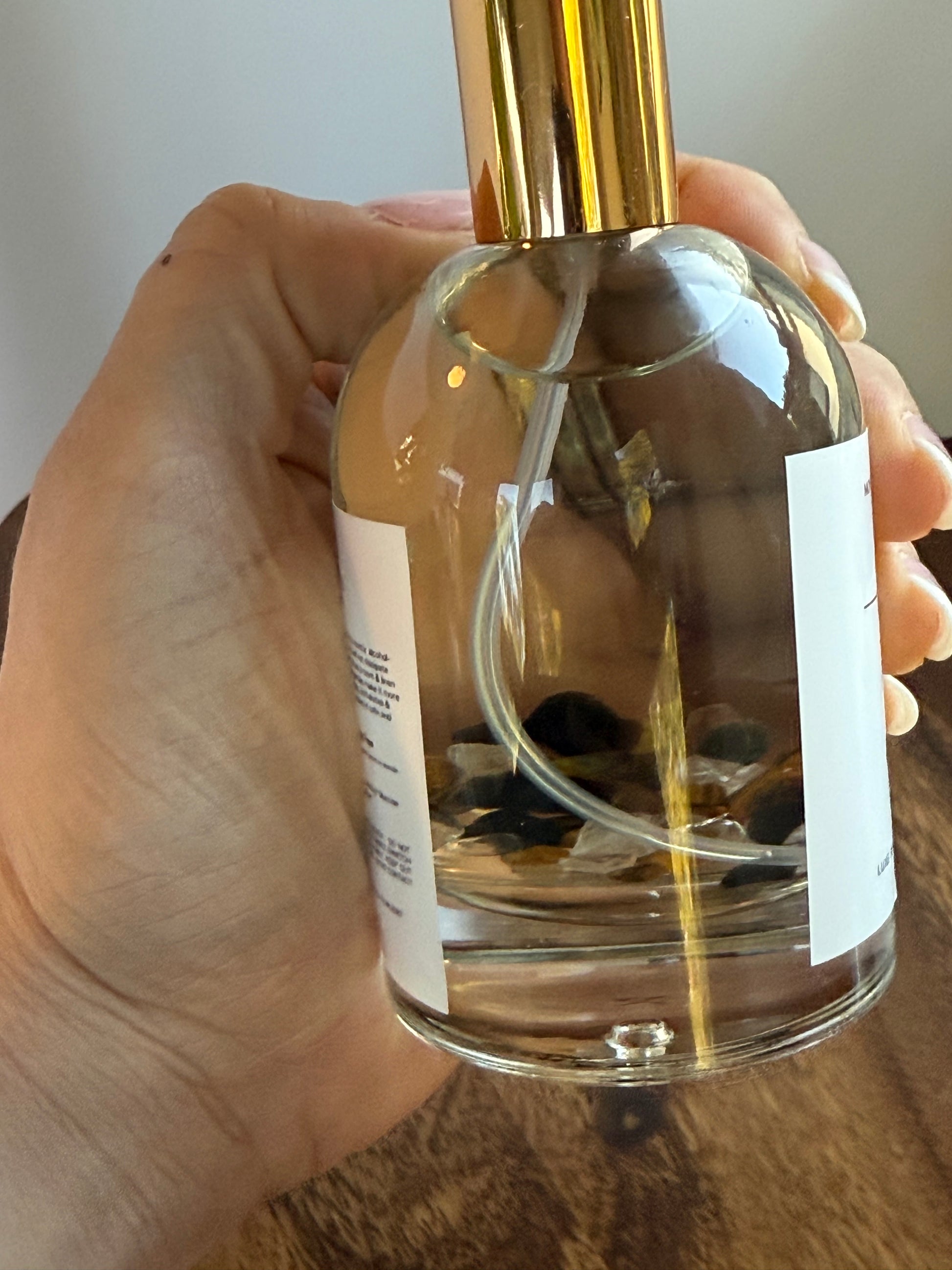 Hand holding a clear glass bottle with a gold cap, filled with a liquid.