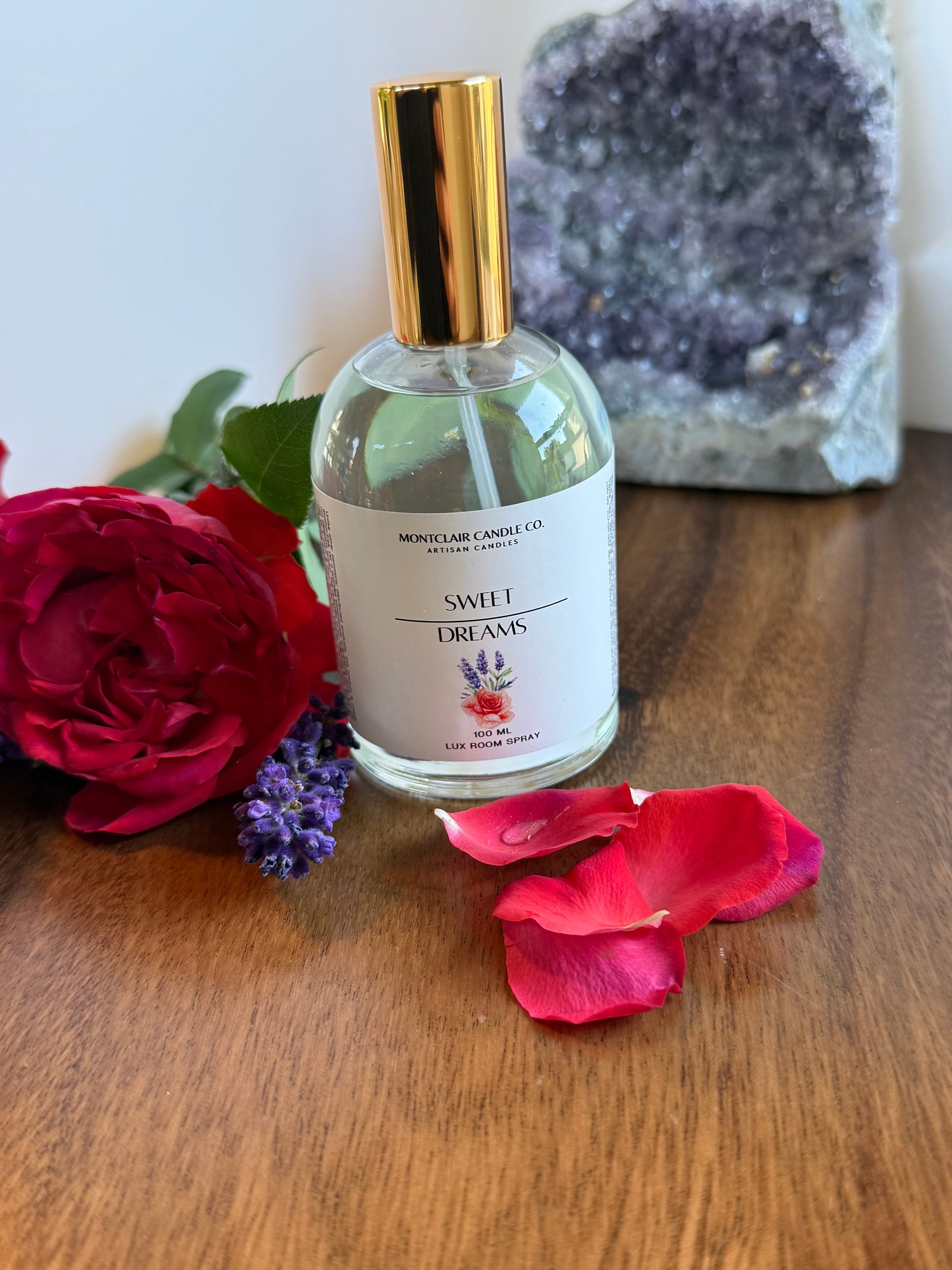 Bottle of perfume with a gold cap on a wooden surface with flowers and crystals.