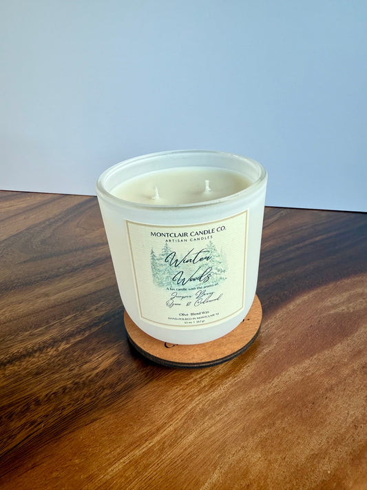 White candle with a label on a wooden coaster against a light blue background